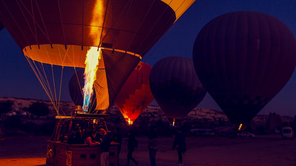 Ground crews inflating hot air balloons on a launch field at dawn near Göreme, with envelopes lying part filled on the ground
