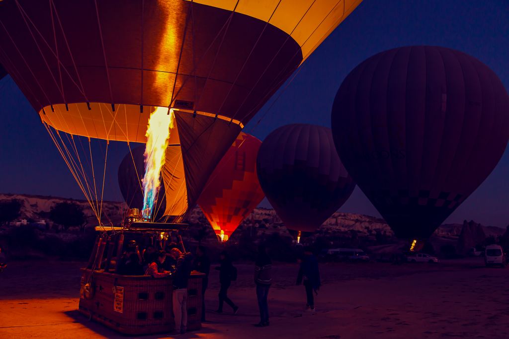 Ground crews inflating hot air balloons on a launch field at dawn near Göreme, Cappadocia, with envelopes lying part-filled on the ground