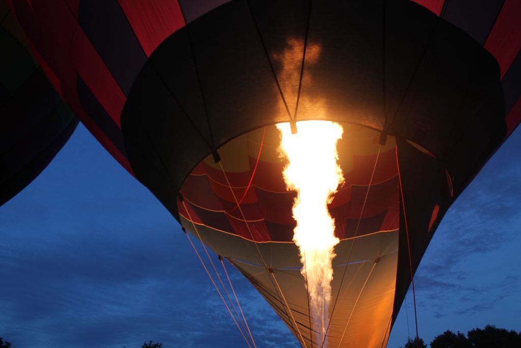 A balloon burner firing into the mouth of the envelope, seen from below, the fabric lit orange by the flame