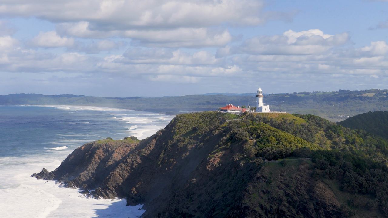 Aerial view of Cape Byron Lighthouse standing on the green cliff headland above the ocean at Byron Bay