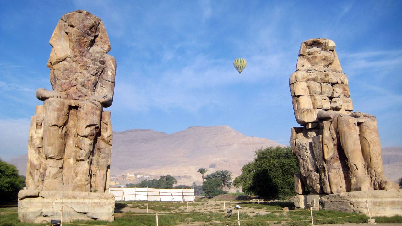 The Colossi of Memnon on the west bank, with a balloon on the morning traffic behind them.