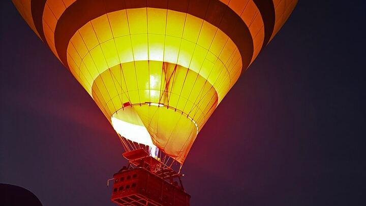 Glowing against the night sky, a hot air balloon rises gracefully as its burner ignites, casting a warm golden light