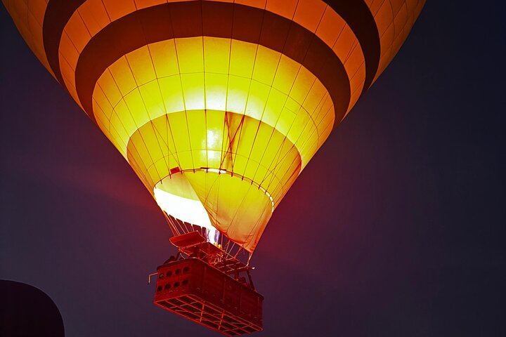 Glowing against the night sky, a hot air balloon rises gracefully as its burner ignites, casting a warm golden light