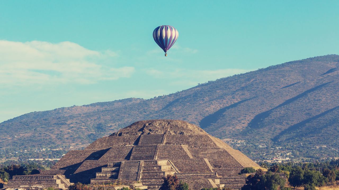 Hot air balloons rising over the Teotihuacan valley in Mexico at first light, with the archaeological zone below