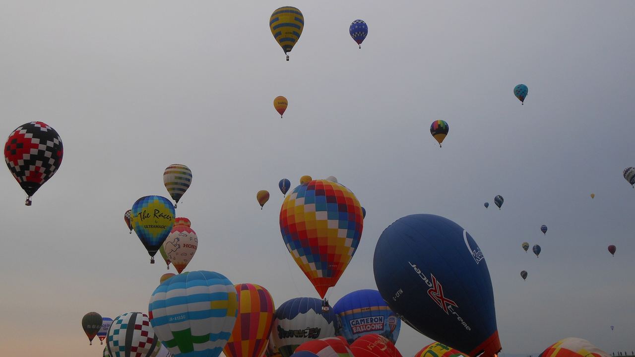 Dozens of hot air balloons lifting off together from the Kase River bank during the Saga International Balloon Fiesta in Japan