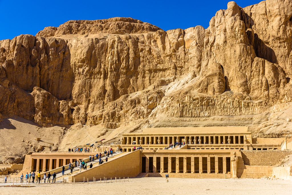 The three terraces of Hatshepsut's temple at Deir el-Bahari below the Theban cliffs, with visitors on the access ramp.