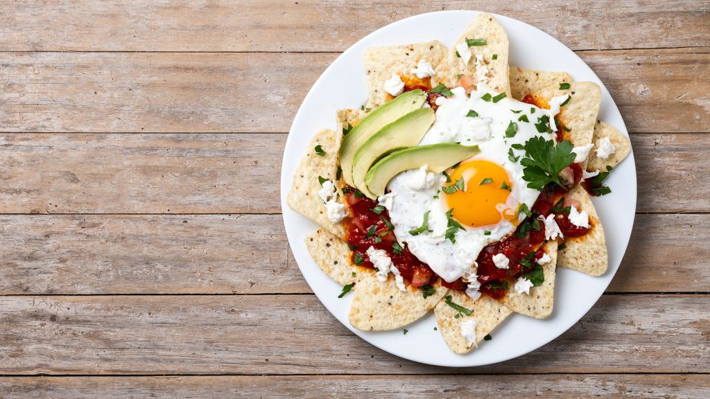 A plate of red chilaquiles topped with a fried egg on a wooden table