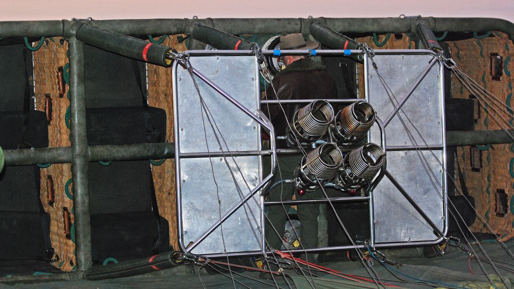 Large hot air balloon basket lying on its side before inflation, showing four padded passenger compartments separated by wicker partitions