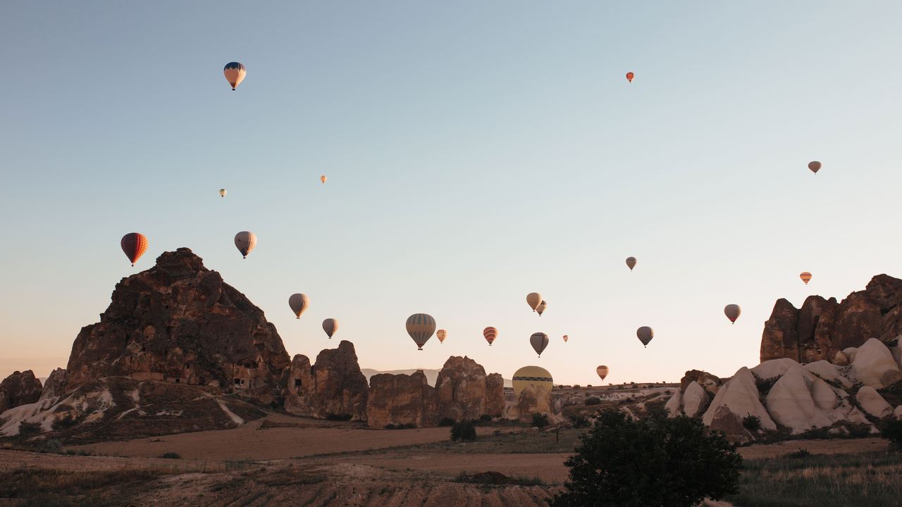 Dozens of hot air balloons airborne together over the rock valleys of Cappadocia at sunrise, at several different heights